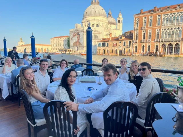 Melanie and her loved ones gathered around a table beside the water in Venice